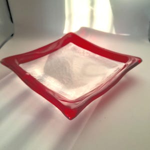 Op de afbeelding: Een vierkante glazen schaal met een rode rand. De schaal is gemaakt van helder glas en heeft een licht getextureerd oppervlak.