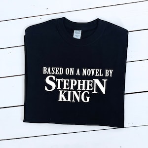 Puede incluir: Camiseta negra con texto blanco que dice "Based on a novel by Stephen King".