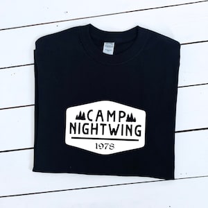 May include: Black t-shirt with a white patch that says "Camp Nightwing 1978" with a silhouette of pine trees.