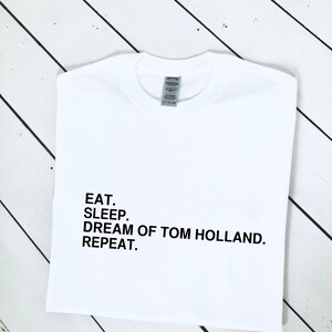 May include: White t-shirt with black text that reads "Eat. Sleep. Dream of Tom Holland. Repeat."