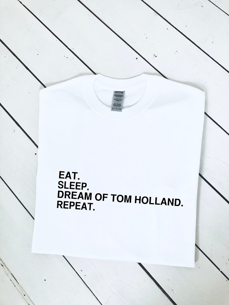 May include: White t-shirt with black text that reads "Eat. Sleep. Dream of Tom Holland. Repeat."