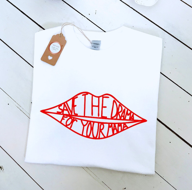 May include: White t-shirt with a red graphic of a pair of lips. The lips are outlined in red and the text "Save the drama for your mama" is written inside the lips.