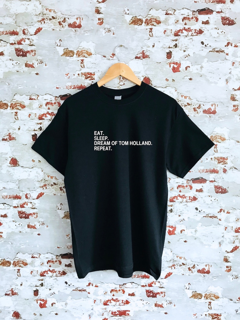 May include: Black t-shirt with white text that reads "EAT. SLEEP. DREAM OF TOM HOLLAND. REPEAT."