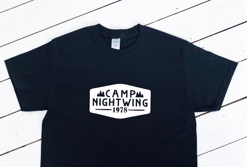 May include: Black t-shirt with a white graphic of a camp logo. The logo says "Camp Nightwing - 1978".