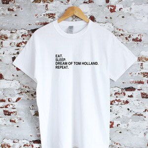 May include: White t-shirt with black text that reads "Eat. Sleep. Dream of Tom Holland. Repeat."