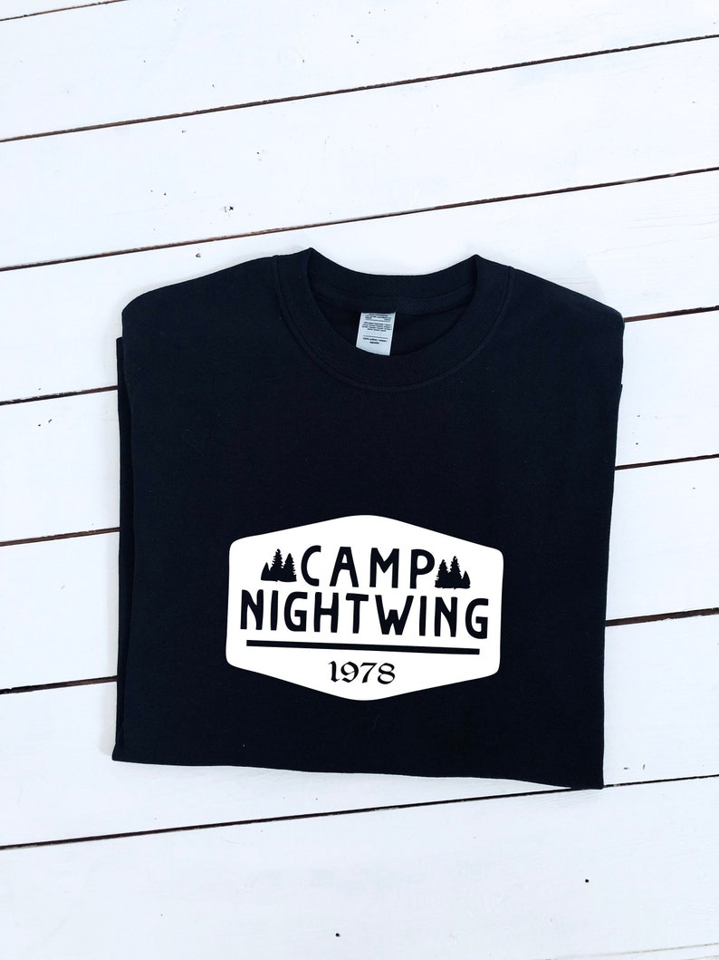 May include: Black t-shirt with a white patch that says "Camp Nightwing 1978" with a silhouette of pine trees.