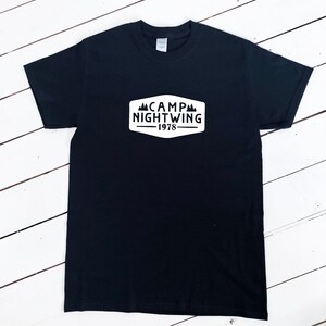 May include: Black t-shirt with a white patch that says "CAMP NIGHTWING -1978" with a mountain graphic.