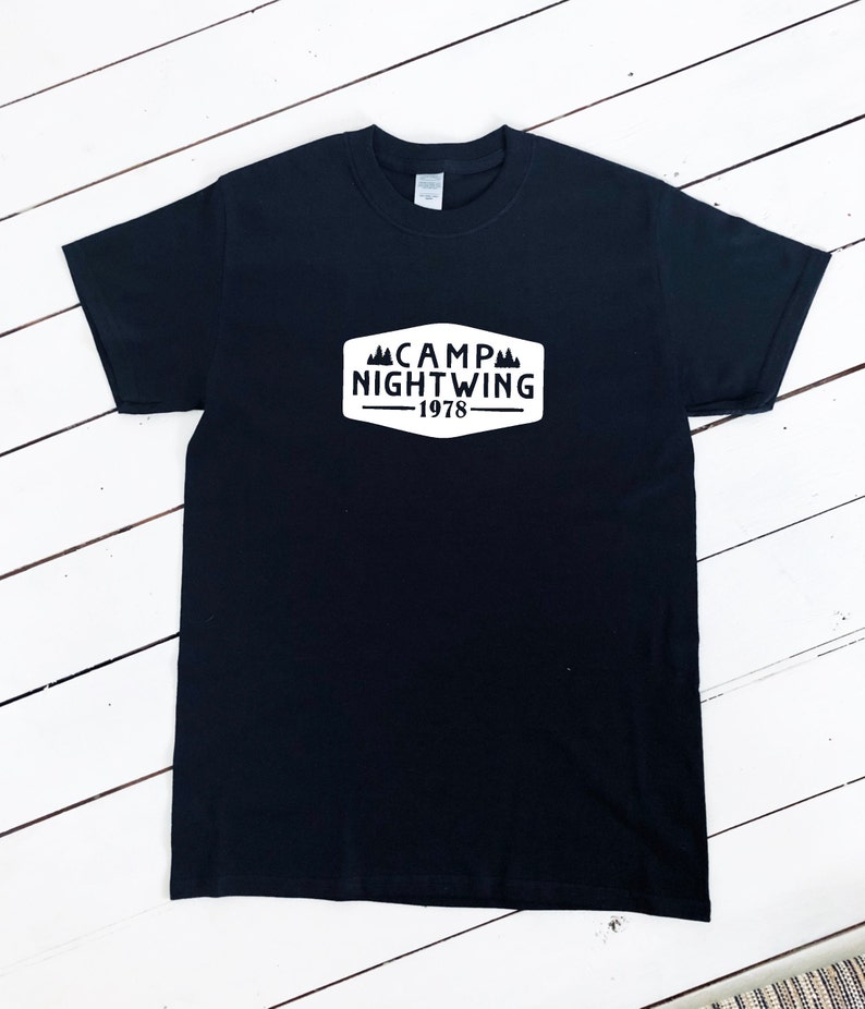 May include: Black t-shirt with a white patch that says "CAMP NIGHTWING -1978" with a mountain graphic.