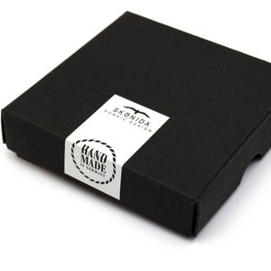 Op de afbeelding: Een zwarte doos met een wit label waarop "Sk&ouml;nida Nordic Design" en "Hand Made in Germany" staat.