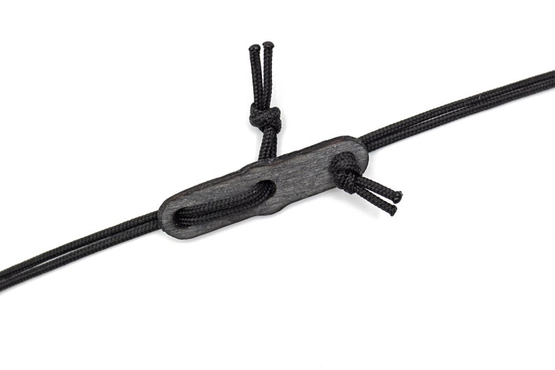 Op de afbeelding: Een zwart leren koord met een houten toggle. Het koord is aan beide uiteinden geknoopt en de toggle heeft een gat in het midden.