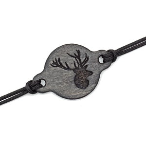 Op de afbeelding: Een zwarte houten armband met een ronde hanger met een gegraveerd hertenkopontwerp. De armband is gemaakt van zwart koord.