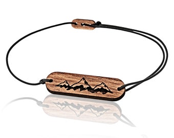 Op de afbeelding: Een houten armband met een zwart koord en een rechthoekige houten bedel met een bergketenontwerp.