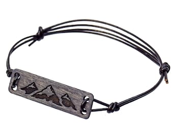 Op de afbeelding: Een zwart leren armband met een houten bedel met een bergketenontwerp.