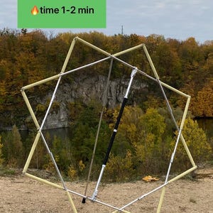 Pode incluir: Uma estrutura metálica dobrável em forma de estrela com pegas texturizadas de cor clara em cada segmento e um punho central preto. Um retângulo verde no topo exibe o texto "time 1-2 min" com um ícone de chama para o tempo.