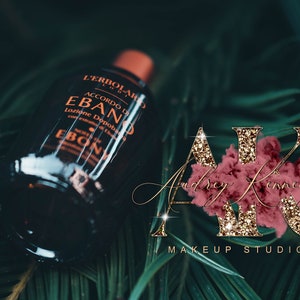 May include: A dark brown glass bottle with a gold label that reads "L'Erbolario Accordo di Ebano Lozione Dopobarba" and "Ebano" in a gold font. The bottle is sitting on a bed of green leaves.