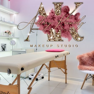 May include: A makeup studio with a white chair and a beige treatment table. The wall has a pink and gold glitter logo that says "AK Makeup Studio" with the text "Audrey Kennedy" in cursive.