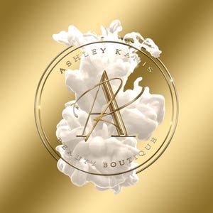 Może przedstawiać: Złote koło z tekstem "Ashley Kanis Beauty Boutique" wok&oacute;ł krawędzi. Litera "A" znajduje się w środku koła i jest otoczona białymi wirami atramentu.