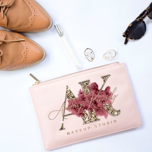 May include: A pink makeup bag with a gold zipper and the text "Audrey Kinley Makeup Studio" with a gold glitter design and a pink and gold floral design.