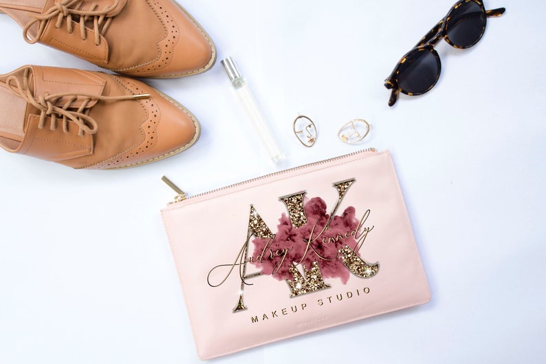 May include: A pink makeup bag with a gold zipper and the text "Audrey Kinley Makeup Studio" with a gold glitter design and a pink and gold floral design.