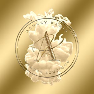 Może przedstawiać: Złote koło z tekstem "Ashley Kanis Beauty Boutique" wok&oacute;ł krawędzi. Litera "A" znajduje się w środku koła, z białym zawirowaniem z tyłu.