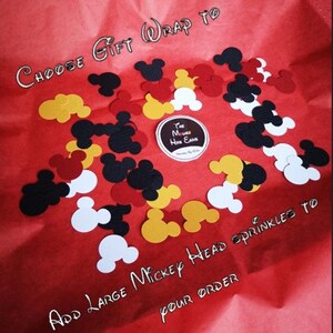May include: Red, yellow, black, and white Mickey Mouse head confetti on a red background. The text "CHOOSE GIFT WRAP TO" and "ADD LARGE MICKEY HEAD SPRINKLES TO YOUR ORDER" is written on the background.