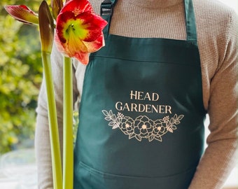 May include: A green apron with a white pocket and the text "HEAD GARDENER" in white with a floral design in gold.