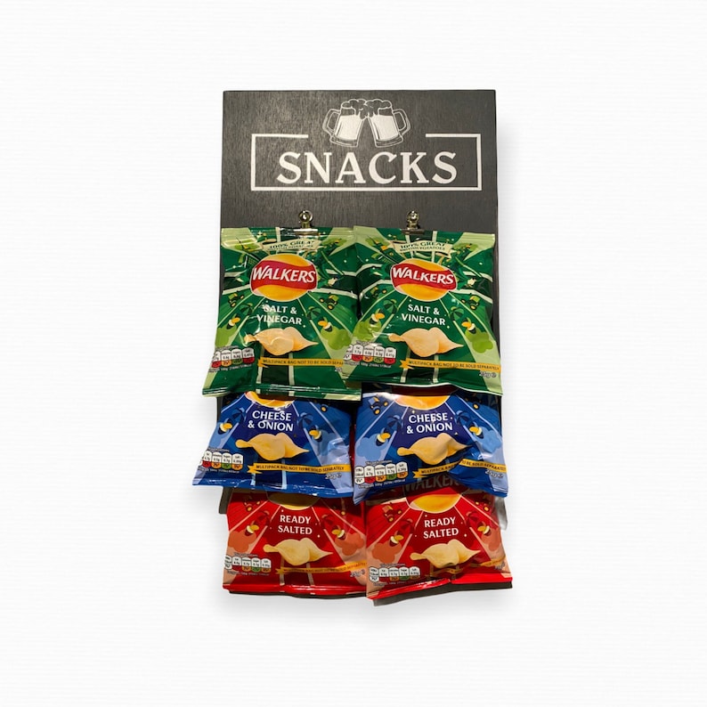 May include: A black wooden sign with the word "SNACKS" in white letters. Six bags of Walker's crisps are displayed on the sign. The bags are in different flavors: Salt & Vinegar, Cheese & Onion, and Ready Salted.