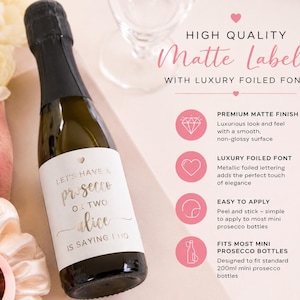 May include: A mini prosecco bottle with a white matte label featuring gold foil text that reads Let's have a prosecco or two Alice is saying I do. The label includes a small heart icon and is designed for 200ml mini prosecco bottles.