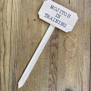 Könnte beinhalten: Ein Holzschild mit dem Text "Mojitos in Training" auf einem Holzgrund.