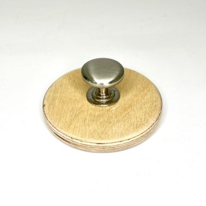 Peut inclure: Un bouton rond en bois avec un bouton en métal argenté sur le dessus. Le bouton est fixé à une base en bois.