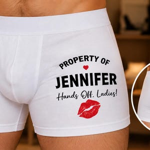 May include: White boxer briefs featuring black text that reads PROPERTY OF JENNIFER, followed by Hands Off. Ladies! and a small red heart and a red lipstick kiss graphic. The garment includes a circular inset showing the plain white back view.