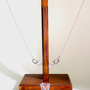 Pu&ograve; includere: Gioco di bicchieri da shot in legno con una catena oscillante e sei porta bicchieri da shot. Il gioco &egrave; in legno scuro e ha un bicchiere da shot in vetro trasparente al centro.