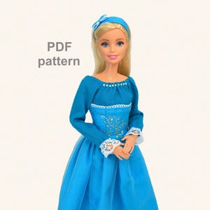 Peut inclure: Une poupée vêtue d'une longue robe turquoise à manches longues et garniture en dentelle blanche. Le corsage est orné de broderies dorées. La poupée a les cheveux blonds et un bandeau turquoise assorti. Le texte "PDF pattern" est visible.