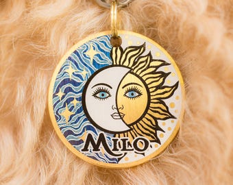 Peut inclure: Médaille pour chien en or avec un motif soleil et lune bleu et blanc. La médaille porte l'inscription "Milo" en lettres dorées.