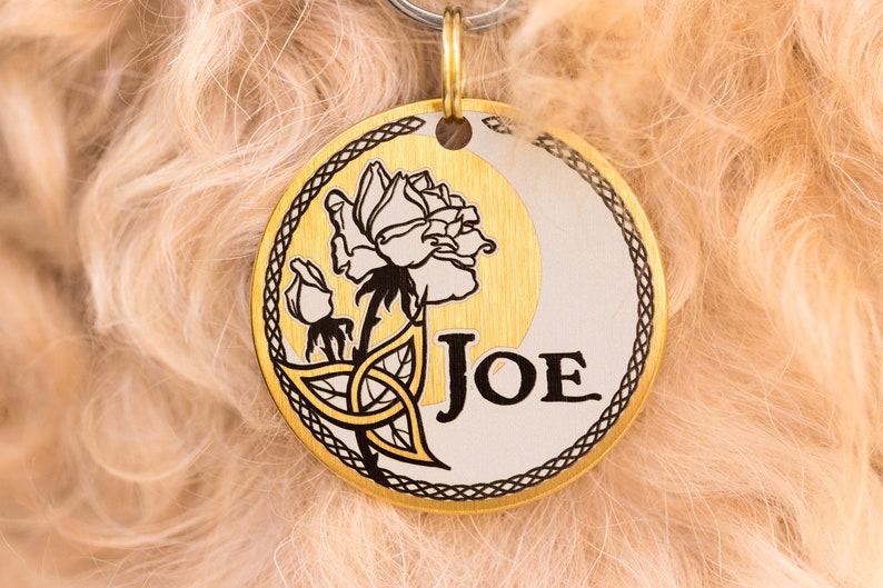 May include: Gold dog tag with a Celtic knot design and a white rose with the name "JOE" engraved on it.