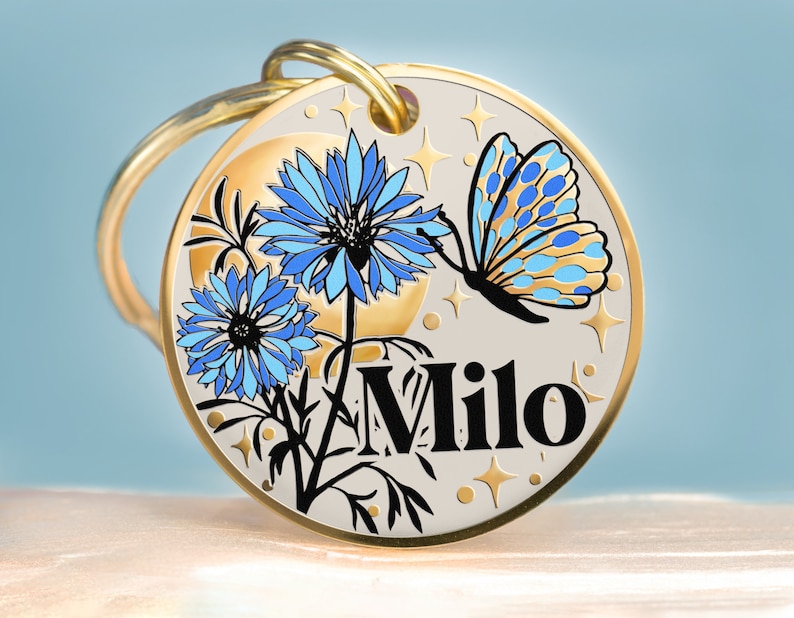 High-quality round dog or cat collar tag featuring an original hand-drawn nature scene—cornflower, sparkling moon, and stars. It looks like a one-of-a-kind miniature painting, created with black ink on a matte white background. The shiny borders, moon, and stars match the tag’s color (silver, gold, or rose gold), creating a playful, eye-catching effect. Artwork is engraved on a stainless steel pendant. Personalized with your pet’s name on the front and your message on the back. Sizes: S,M,L.