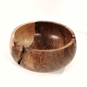 Puede incluir: Un tazón de madera grande y redondo con un acabado de madera natural. El tazón tiene un patrón de veta único y una pequeña grieta en el lateral.