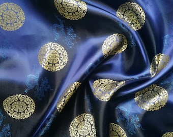 Könnte beinhalten: Nahaufnahme eines marineblauen Satinstoffs mit goldenen kreisförmigen Mustern und blauen Drachenmotiven. Der Stoff hat einen glänzenden Glanz und ist drapiert, wodurch Schatten und Lichteffekte entstehen.