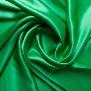May include: A close-up shot of emerald green satin fabric. The fabric is draped and swirled, creating soft folds and shadows. The shiny material reflects light, highlighting the smooth texture. This textile is suitable for apparel and home decor.