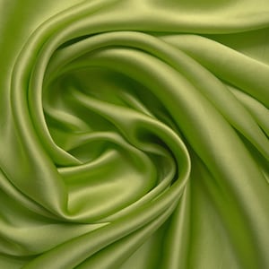 May include: Close-up of a vibrant, lime green fabric with a silky sheen. The material is draped and swirled, creating soft folds and shadows. The fabric's smooth texture and bright color suggest it could be used for apparel or home decor.