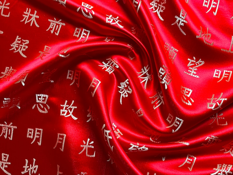 K&ouml;nnte beinhalten: Ein leuchtend roter Satin-Stoff mit einem Wirbelmuster. Der Stoff ist mit goldenen chinesischen Schriftzeichen verziert. Der Satin hat einen gl&auml;nzenden Glanz, und die Falten erzeugen Schatten, die dem Design Tiefe verleihen.