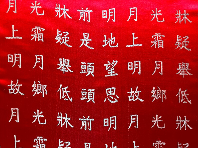 K&ouml;nnte beinhalten: Roter Stoff mit wei&szlig;en chinesischen Schriftzeichen, die auf der Oberfl&auml;che gestickt sind. Der Text ist in vertikalen Spalten angeordnet und wird von oben nach unten, von rechts nach links gelesen. Der Stoff hat einen leichten Glanz.