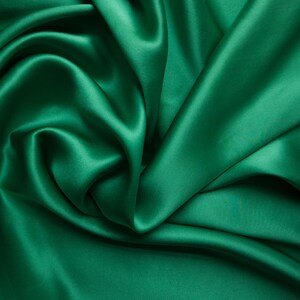 May include: Emerald green satin fabric with soft folds and a lustrous sheen. The fabric is draped, creating a flowing, textured appearance. Ideal for apparel, home decor, or craft projects.