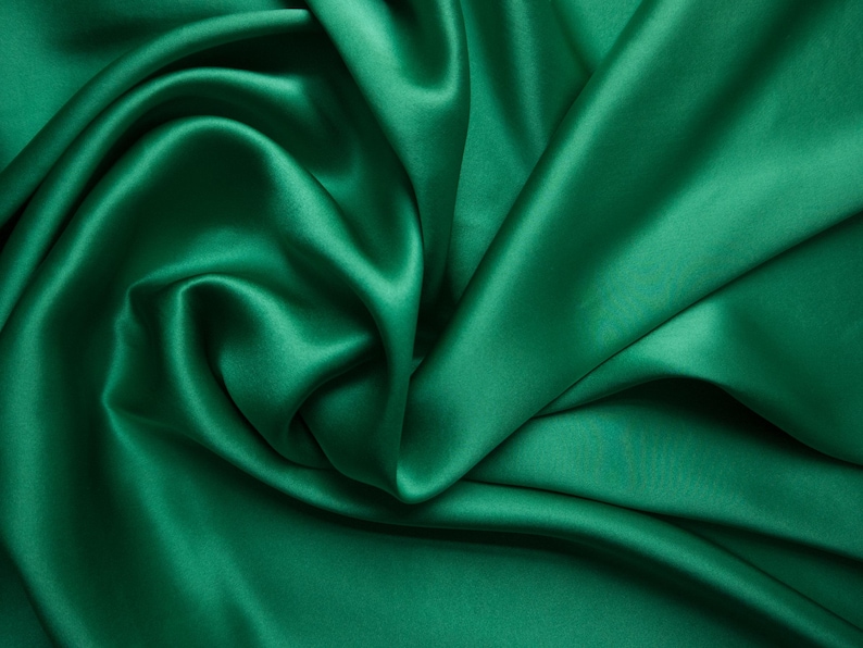 May include: Emerald green satin fabric with soft folds and a lustrous sheen. The fabric is draped, creating a flowing, textured appearance. Ideal for apparel, home decor, or craft projects.