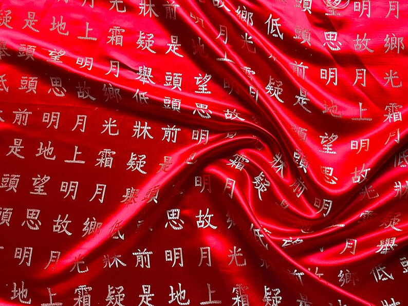 K&ouml;nnte beinhalten: Ein leuchtend roter Satin-Stoff mit flie&szlig;ender, drapierter Textur. Der Stoff ist mit silbernen chinesischen Schriftzeichen verziert, die ein Muster auf der Oberfl&auml;che bilden. Die Beleuchtung hebt die Falten und den Glanz des Materials hervor.