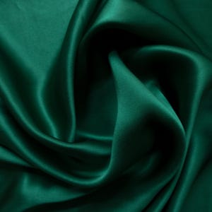 May include: Close-up of emerald green satin fabric with soft folds and a lustrous sheen. The fabric's smooth texture and rich color create a luxurious appearance. Ideal for apparel, home decor, or craft projects.
