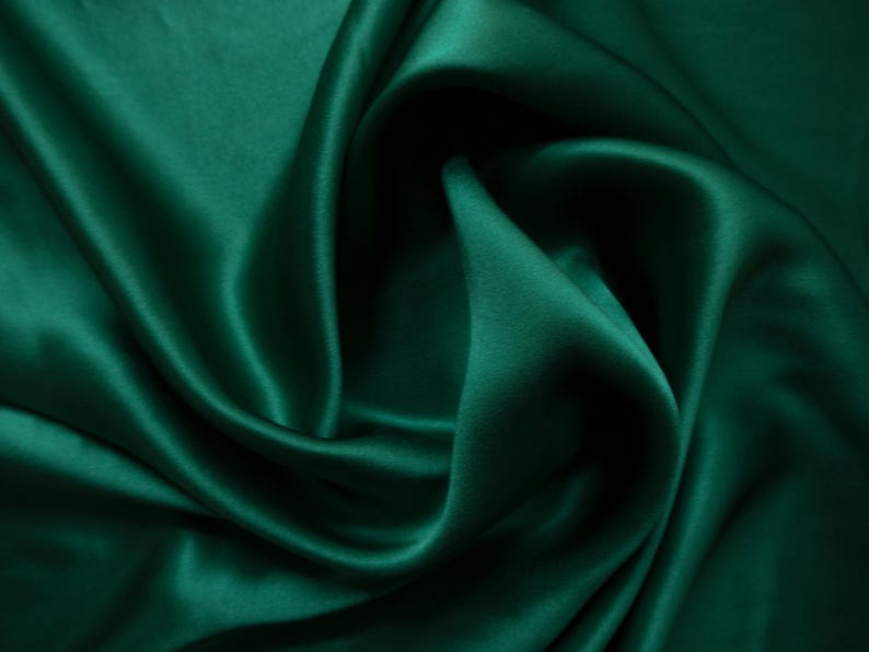 May include: Close-up of emerald green satin fabric with soft folds and a lustrous sheen. The fabric's smooth texture and rich color create a luxurious appearance. Ideal for apparel, home decor, or craft projects.
