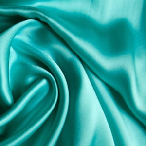 May include: Close-up of a turquoise satin fabric with soft folds and a lustrous sheen. The fabric's smooth texture and vibrant color create a luxurious appearance. Ideal for apparel, home decor, or craft projects.