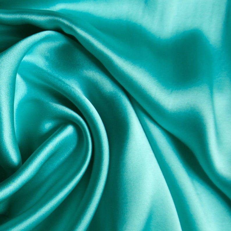 May include: Close-up of a turquoise satin fabric with soft folds and a lustrous sheen. The fabric's smooth texture and vibrant color create a luxurious appearance. Ideal for apparel, home decor, or craft projects.