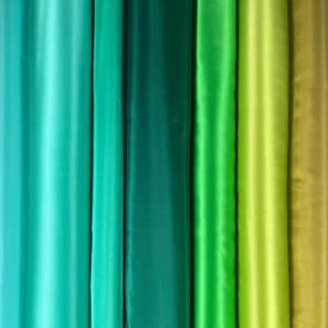 May include: A vertical display of various shades of green fabric. The colors range from a light teal to a deep forest green, with a few shades of lime and olive green. The fabric appears to be a smooth, satin-like material.